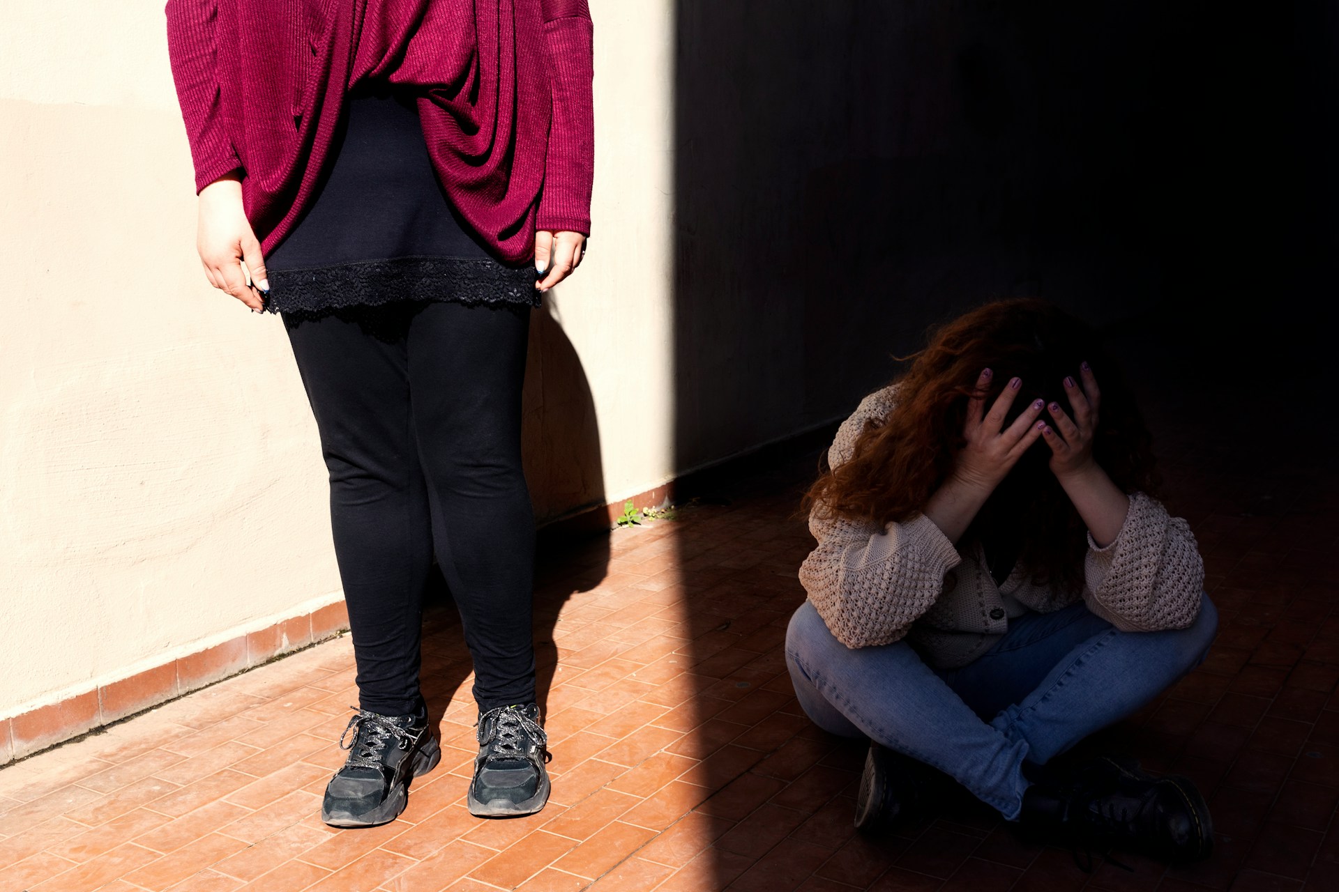 a kép bal oldalán egy nő deréktól lefelé erős napsütésban, a jobb oldalon sötétben gubbasztó kislány